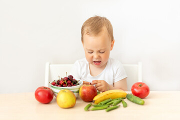 baby boy 2 years old sitting at a table on a white isolated background and eating fruits vegetables, baby food concept, place for text