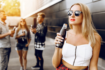 Closeup of a beautiful blonde girl with a glass drink, in the background a group of friends having fun