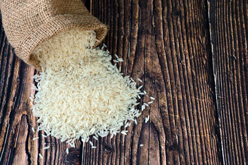  White rice spill out of the burlap bag on the wooden table