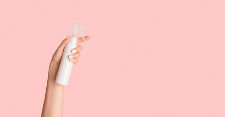 Unrecognizable young lady holding white sprayer bottle with cosmetic product against pink...