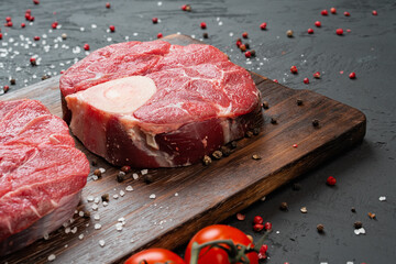 Two raw fresh marbled meat steak on dark background, cherry tomatoes and spices.