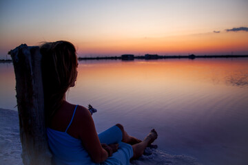 Rear view of the woman back silhouette look to the purple sunrise in water on summer. Woman sit on the shore of the salt beach at pink lake. vacation lifestyle near ocean