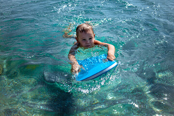 The child teaching to swimm with special equipment . The kid holding the kickboard and try do sweam on the shore of the beach in the sea