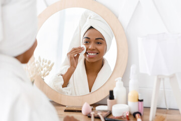 Fototapeta premium Beauty Routine. Beautiful african girl cleaning face with cotton pad at home,