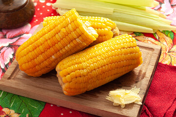 boiled corn with butter on wooden board and colorful table and straws