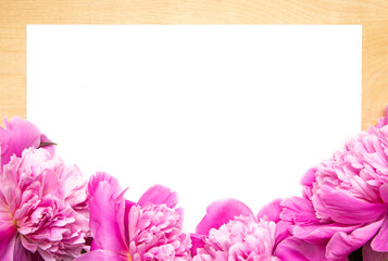 White paper card on rustic wooden background with pink peonies. Flowers. Workspace. Blank for greetings