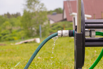 Daylight. in focus the fitting drips water from it. Near a hose reel