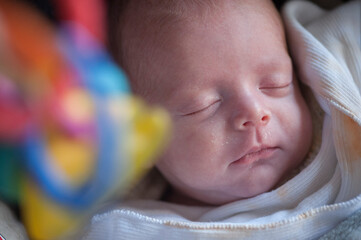 A two months old premature boy sleeping, with a colorful toy blurred in the foreground