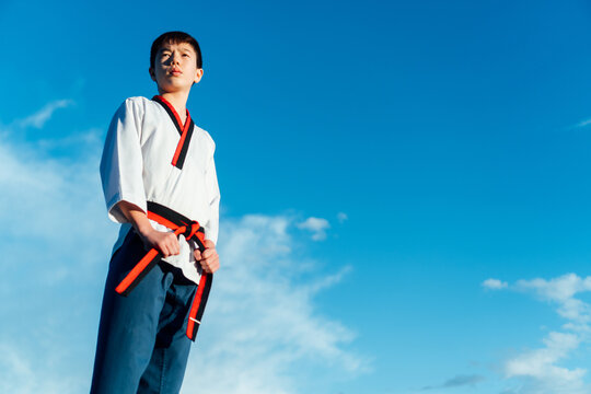 Portrait of a young Japanese man in his taekwondo kimono holding the black belt of his martial arts kimono. White kimono and blue karate pants