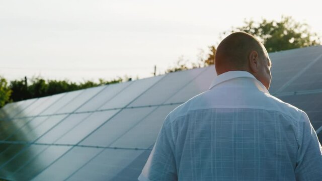 Back view: Home power plant owner walks along row of solar panels