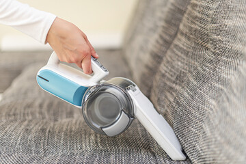 Woman vacuuming furniture in a house with a hand-held portable vacuum cleaner.