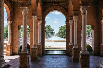View of the fountain in Plaza de España between the arches on a sunny day, Seville, Andalucia Horizontal photograph