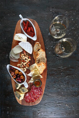 Snacks for wine in the assortment. Cheese and cold cuts with nuts on a wooden Board. Textured aged dark background. Copy of the space. Top view.