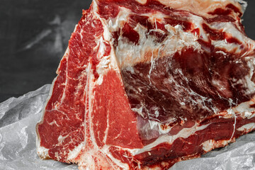 Raw T-bone steak cooking on stone dark table.