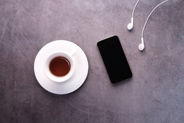 Fototapeta na wymiar smart phone with empty screen, tea and earphone on gray background 