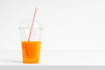 Take away plastic glass of fresh orange juice with a lid and a straw on a white wooden table. Copyspace.