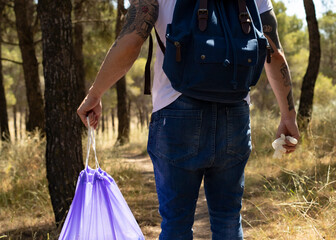 man with a backpack, gloves and garbage bag, collecting plastic from a forest