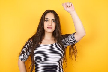 Young pretty Caucasian brunette woman feeling serious, strong and rebellious, raising fist up,...