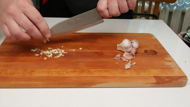 A man finely cuts garlic with a Japanese santoku knife with a wooden board, close-up