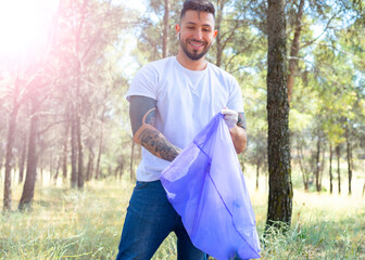 Volunteer man collecting plastic bottles in a forest, in garbage bag, ecology