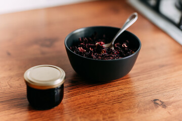Loose tea in black bowl with spoon. Little honey can on the wooden table. Bright kitchen interior. Wooden complete kitchen with gas oven