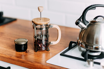 Loose hibiscus tea in french press. Metallic teapot on the gas oven. Bright kitchen interior. White modern dining room. Wooden complete kitchen with gas oven.