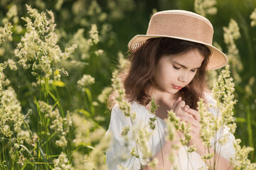 The portrait of a  cute thoughtful girl in a straw hat in a summer morning. Cheerful female kid in straw hat and white dress enjoying vacation spending time.