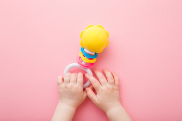 Baby girl hands playing with colorful rattle on light pink floor background. Pastel color. Closeup....