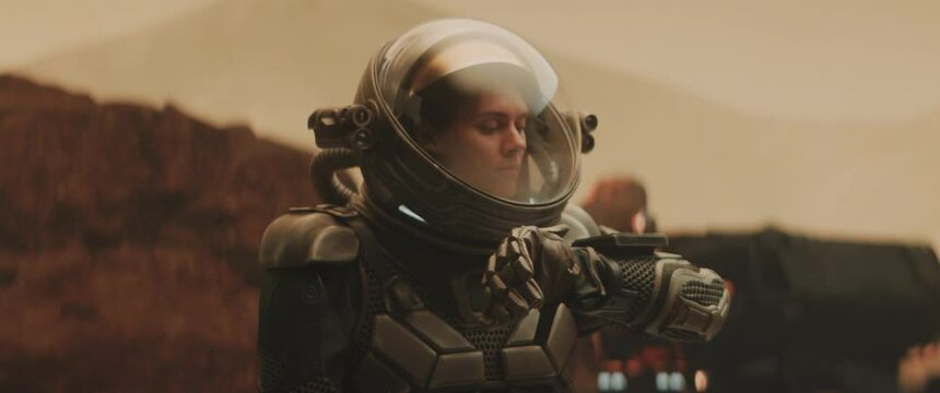 Caucasian female astronaunt checking hud on her suit while exploring planet surface, Mars rover in the background