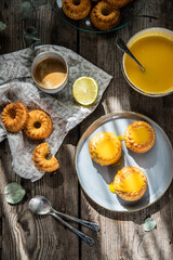 Shaped mini bundt cakes filled with lemon curd and cup of coffee on old wooden table.