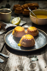 Shaped mini bundt cakes filled with lemon curd and cup of coffee on old wooden table.