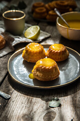 Shaped mini bundt cakes filled with lemon curd and cup of coffee on old wooden table.