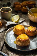 Shaped mini bundt cakes filled with lemon curd and cup of coffee on old wooden table.