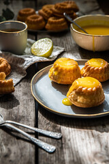 Shaped mini bundt cakes filled with lemon curd and cup of coffee on old wooden table.