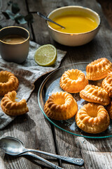 Shaped mini bundt cakes with lemon curd and cup of coffee on old wooden table.