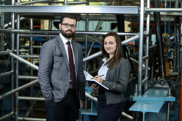 Portrait of a solid businessman with his secretary holding blue notebook, talking about factory financial report in a airplane manufactory. Factory managers controlling work process in a factory