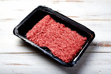 Minced meat in packaging on a light wooden background.