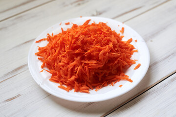 Grated carrots on a plate on a light wooden background.