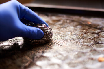 Cleaning a dirty oven pan with a metal sponge and detergent.