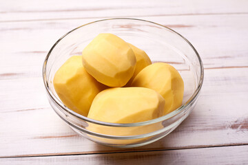 Peeled potato tubers in a plate on a light wooden background. Preparing potatoes for cooking.