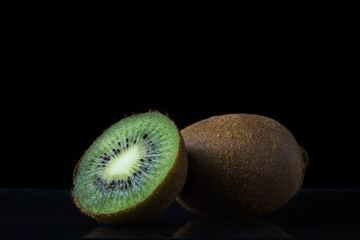 Obraz premium Two kiwi on a black background. One kiwi is whole, the other is cut in half. exotic fruit.