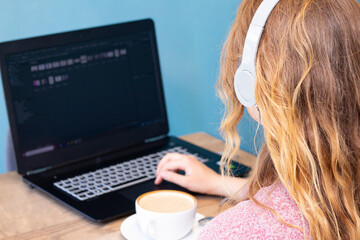 girl with blond hair in headphones working for a laptop and drinking latte