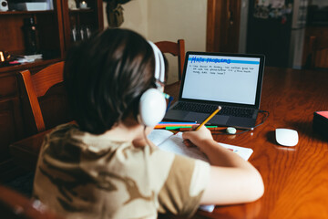 Boy with white headphones doing math homework on his laptop.