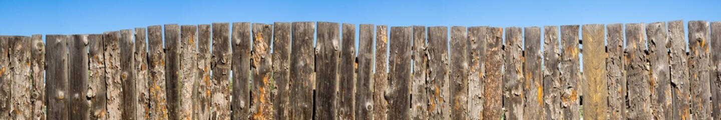 Old wooden fence and blue sky. A crooked fence made of rotten planks. Panorama of the fence for the...