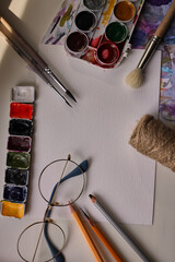 Composition from art materials. Watercolor. Watercolor paints. Stretching paint colors. Art materials. Multi-colored paints. Paint brushes. Pencils and brushes. Sheet of watercolor paper.