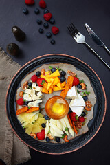 Cheese plate with honey on a dark background. Selection of cheeses. Appetizer with wine. Vertical photo.Copy of the space. Top view.