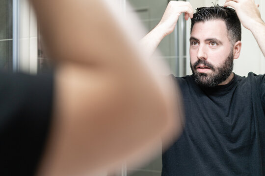 Self haircut. A man is combing his hair in the bathroom