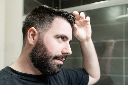 Self haircut. A man is combing his hair in the bathroom