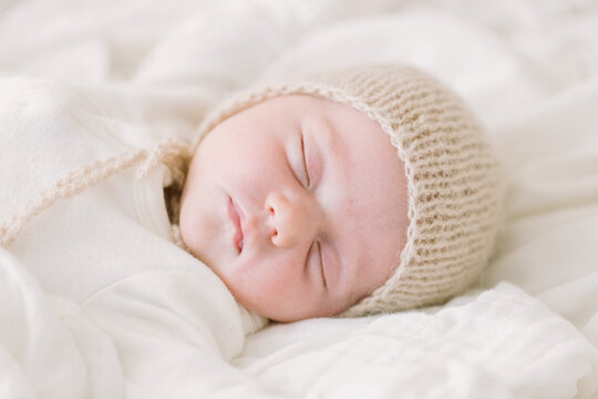 Newborn baby in knit bonnet sleeping on white bed