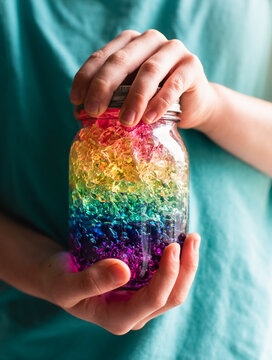 Close up of child's hands holding a jar of rainbow colored crystals.